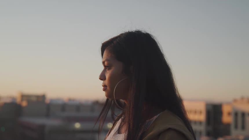 Woman stands on a balcony looking at the sunset on the city
