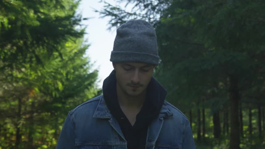 Young man wearing beanie and denim jacket walks on a road through the forest