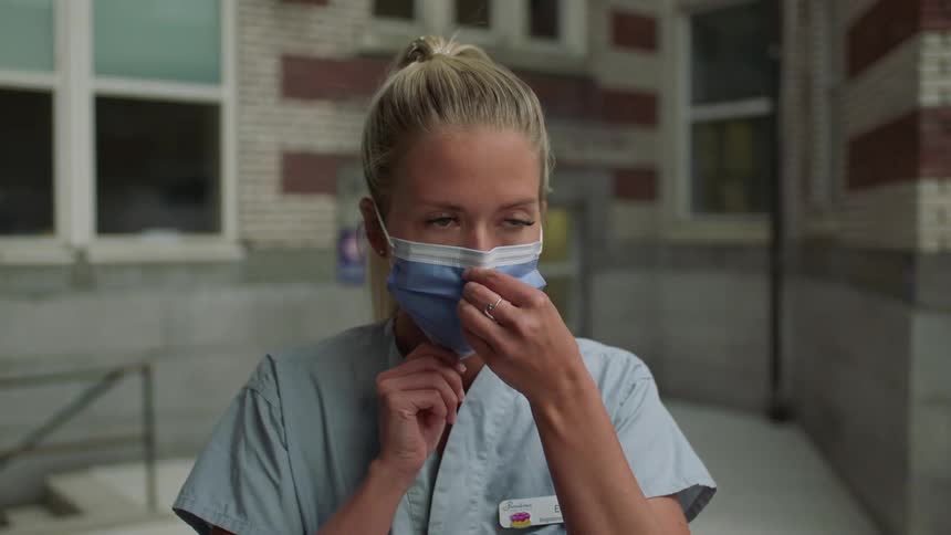 A nurse in scrubs puts on a surgical mask