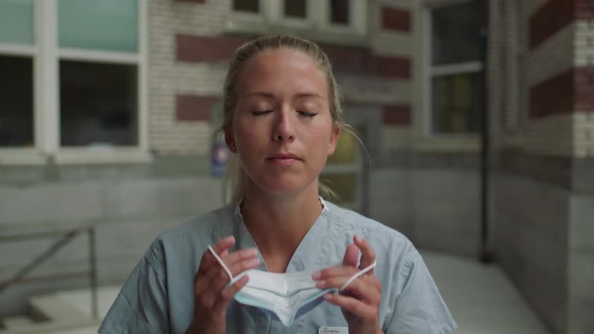 A white female medical worker removes a face mask while standing outdoors