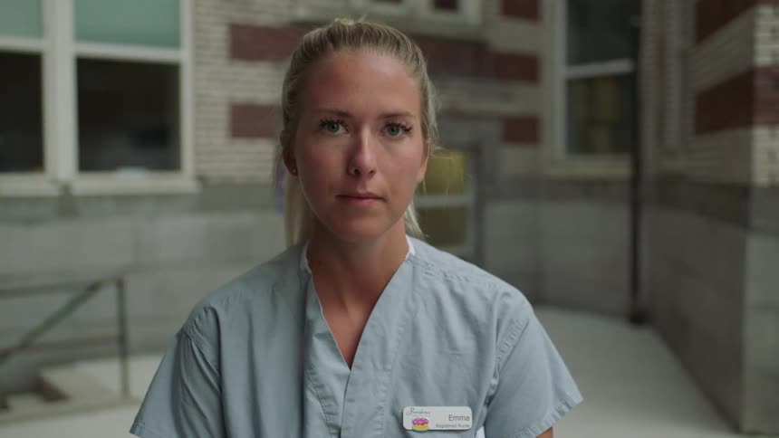 A nurse raising her head to look into the camera while standing outside a hospital