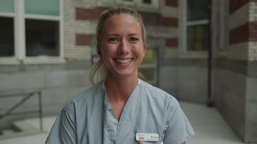 A woman with scrubs and a name tag standing and smiling