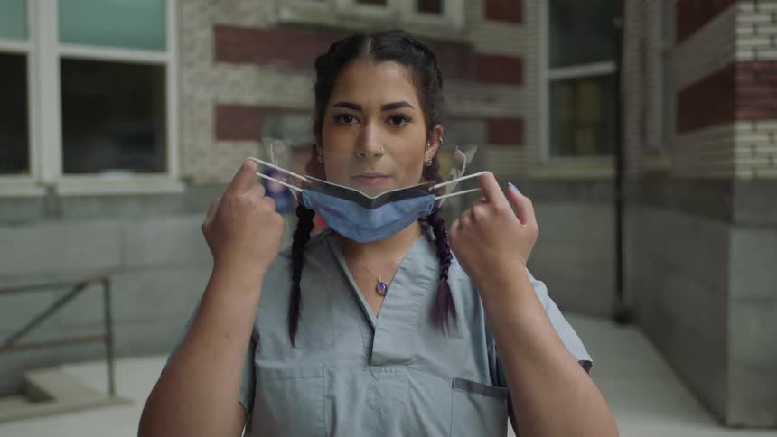 A woman with scrubs taking off a disposable mask