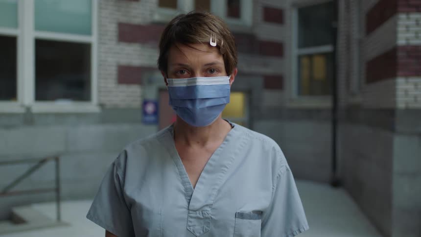 A white female medical worker wears a face mask while standing outside a building