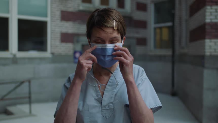 A woman with scrubs putting on a disposable mask