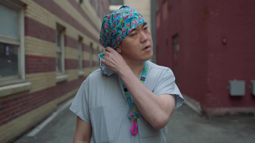 A doctor stands outside and takes his mask off