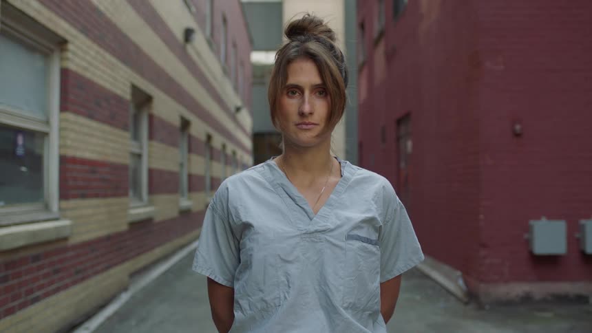 A woman with scrubs looking up with buildings in the background