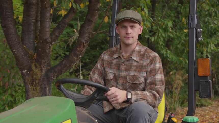 A farmer poses on his green tractor parked next to a tree