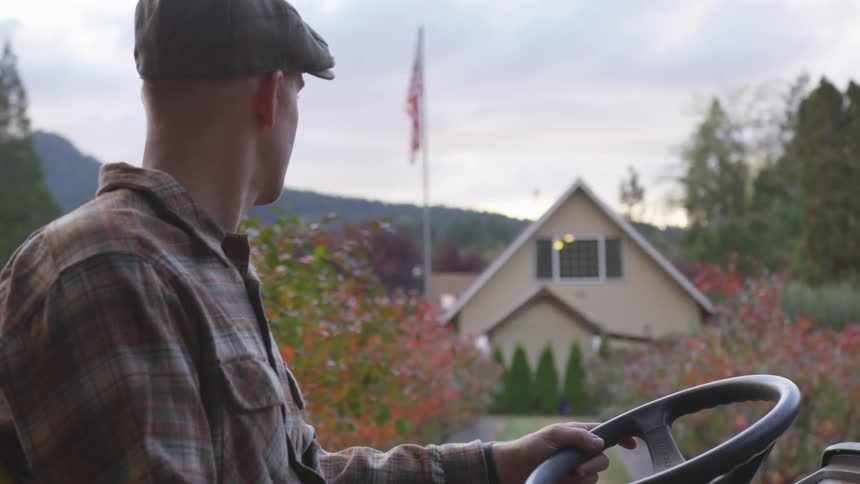 A man sits on an open vehicle looking to a farmhouse in the distance