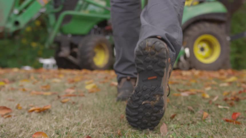 A man walks across a leave covered yard toward a tractor