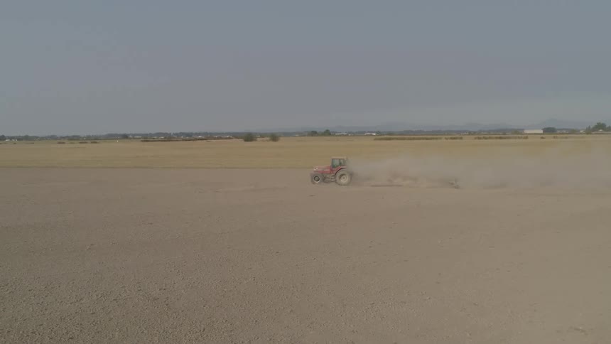 Dust kicks up as a tractor pulls a trailer through a large dirt and gravel field