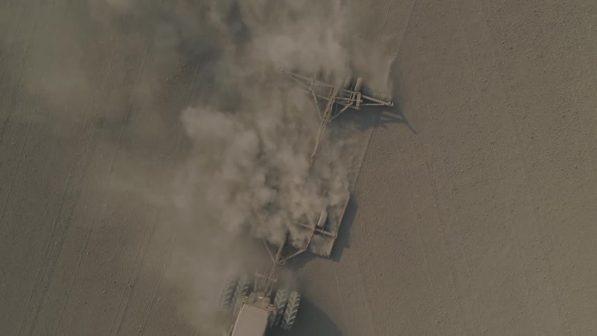Tractor pulling farm equipment through barren field kicking up large dust clouds