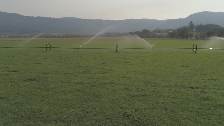 Large sprinklers are used to water crops in a field near a mountain range