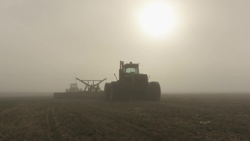 A tractor on a field with the sky clouds and the sun in the background