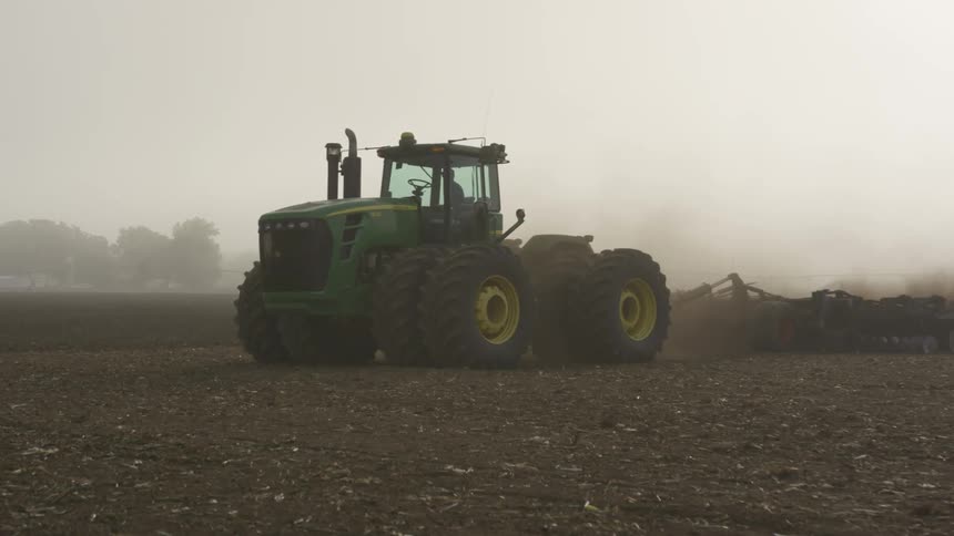 Green tractor ploughing field in a cloud of dust