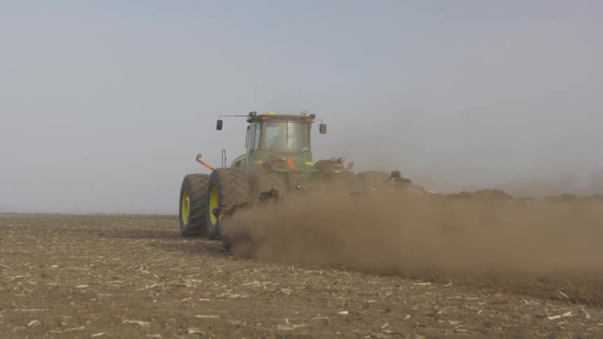 A person driving a tractor across farmland