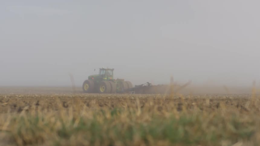 A tractor driving across a field with crops on a farm