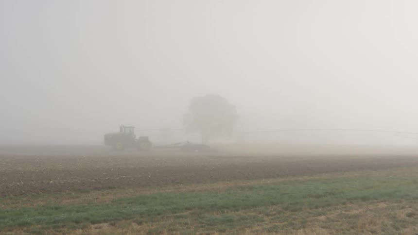 Tractor drives across field under heavy fog