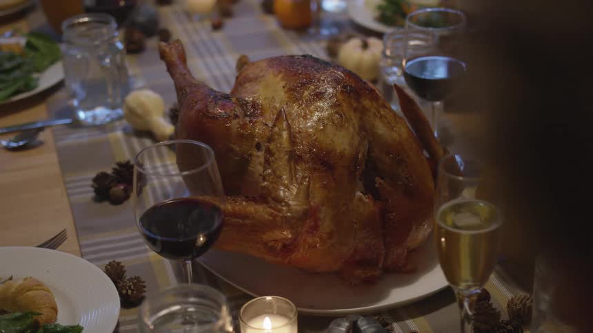 A table is filled with glasses plates and a fresh roasted turkey