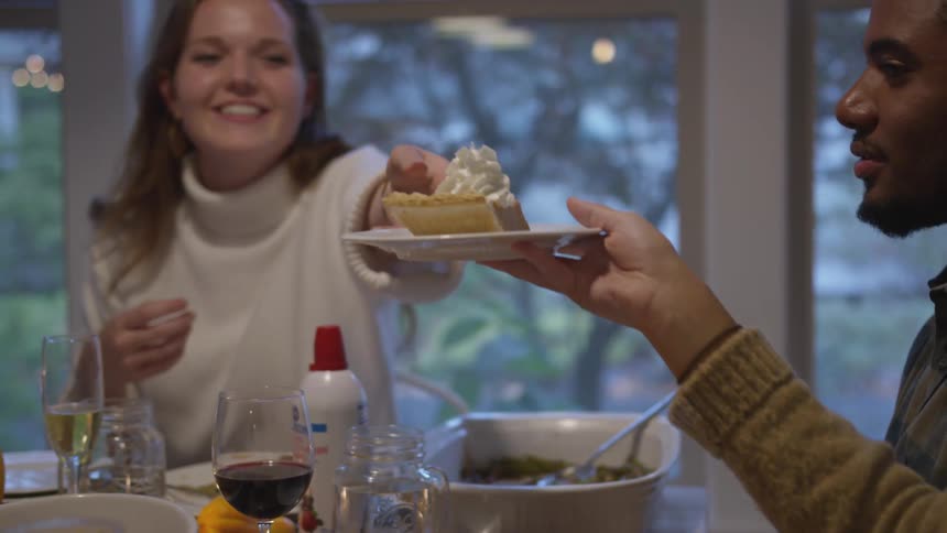 A woman passes a piece of pie to another person at a dinner table