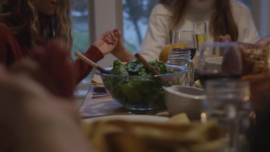 A group of friends sitting at a table holds hands and prays before eating dinner