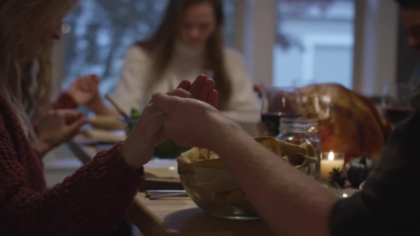 A group of friends sitting at a table holds hands and prays before eating dinner