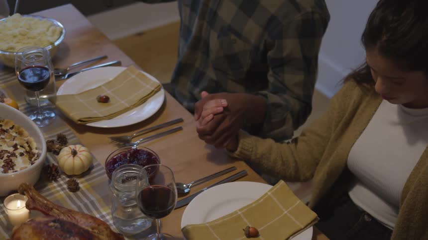 Couple hold hands in prayer at thanksgiving dinner table