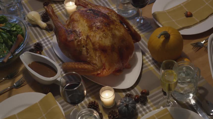 A turkey and other dinner items sit on a table by candles and glasses of wine