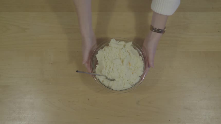 A person sticks a spoon in a bowl of mashed potatoes before lifting the bowl and carrying it away