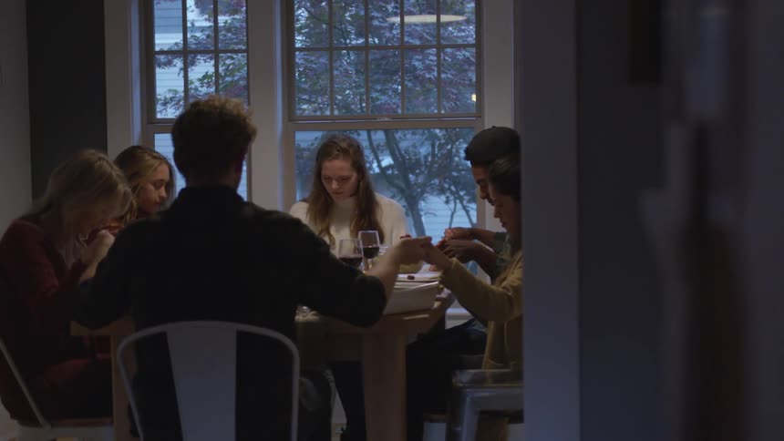 A group of friends sitting at a table holds hands and prays before eating dinner