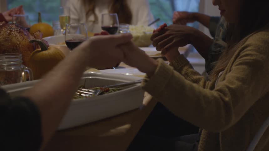 A group of people hold hands and pray as they sit around a table