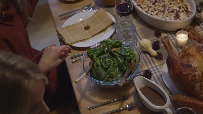 A group of friends sitting at a table holds hands and prays before eating dinner