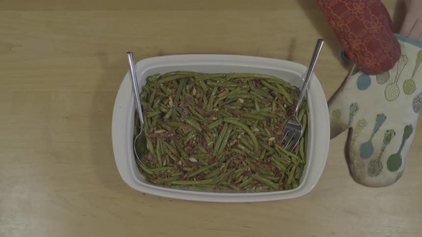 A woman puts on oven mitts and grabs a dish of green bean casserole