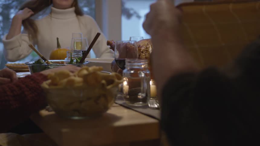 A group of people sit together at a home dinner table and pass food bowls