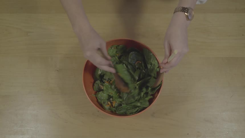 A woman at home stirs a salad