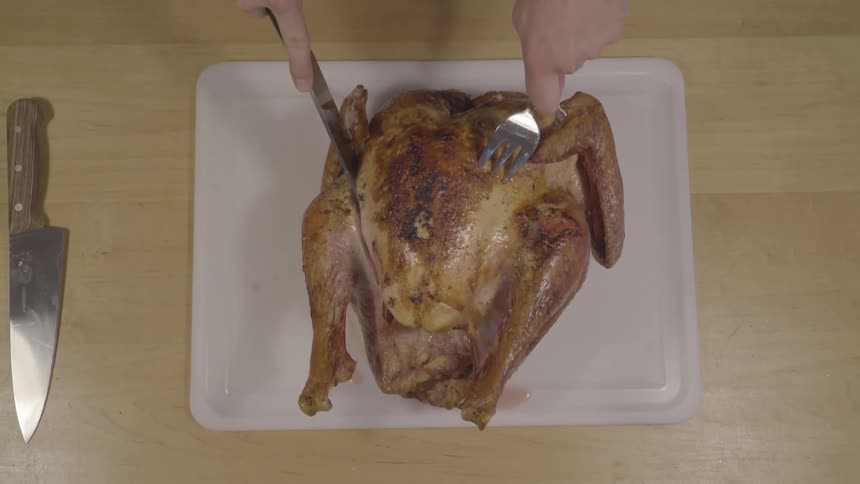 A person uses a large knife and fork to cut through a cooked turkey