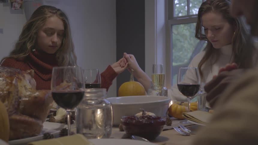 A group of people hold hands as they sit around a table and pray