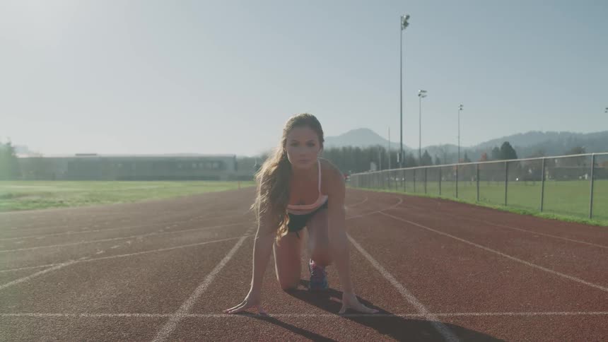 A young female runner crouches down on a running track as she prepares to run