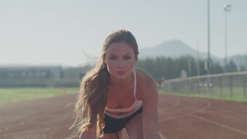 A white girl with long brown hair in a ponytail is bending down on a track looking ahead
