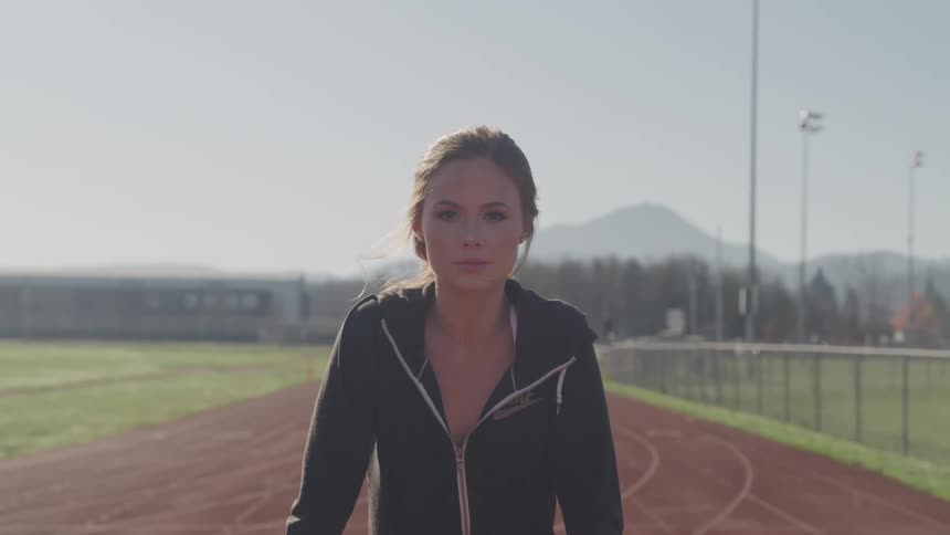 A woman raising her head to look into the camera while standing on an outdoor athletics track on a sunny day