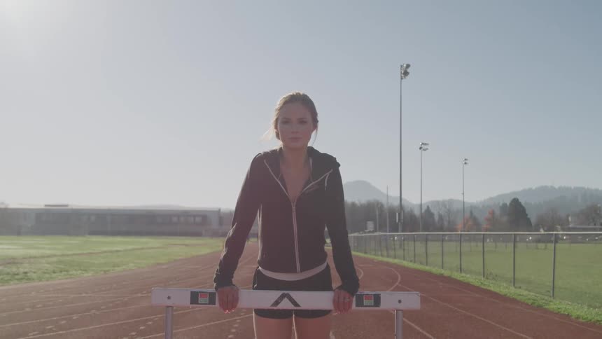 A female athlete stands by a hurdle on a track and field