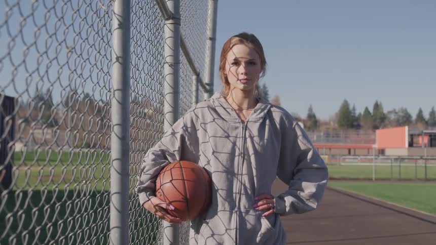 A teenage girl standing on a track holds a basketball