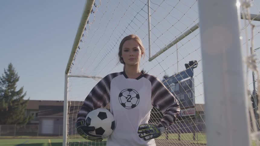 A woman holds a soccer ball while standing in a soccer goal