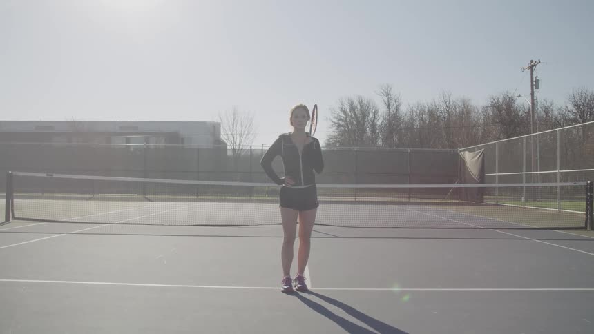 A woman stands on a tennis court holding a tennis racket
