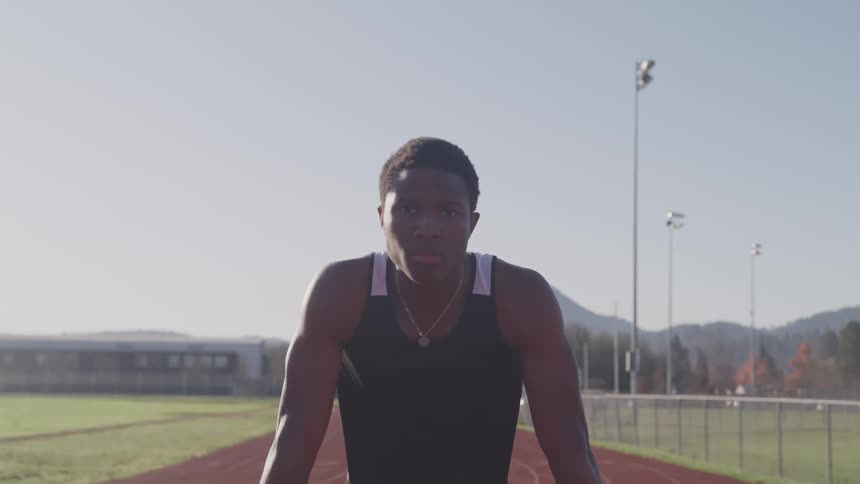 A young black male in athletic apparel poses while on a running track