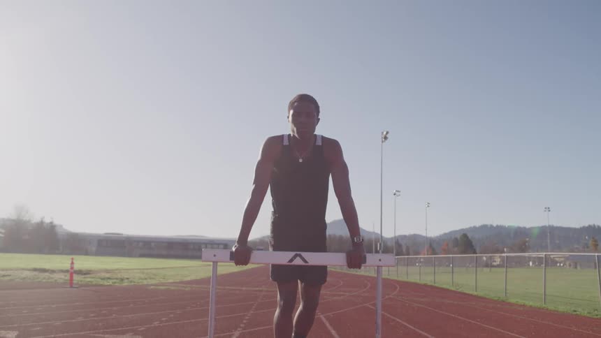 Man wearing sports clothing leaning on a hurdle in an olympic track at sunrise