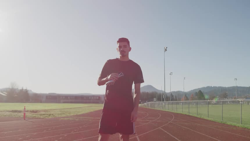 A man stands on a track and field holding his sneakers