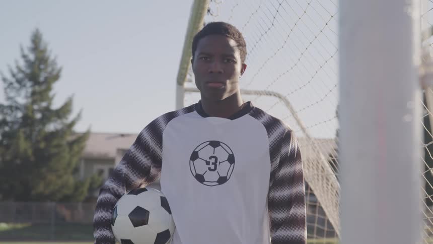 Teenager in soccer jersey holding ball turns to camera