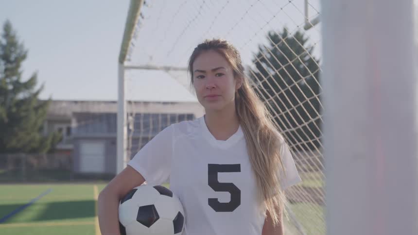 Woman holding soccer ball stands near soccer goal on soccer field