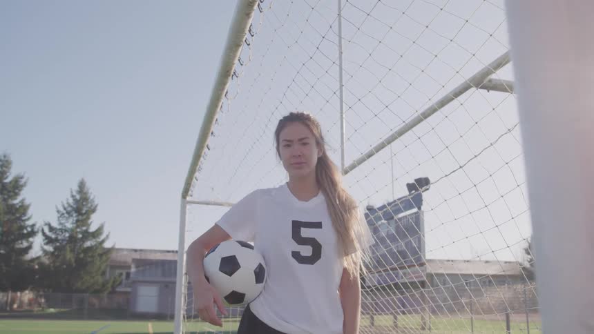A woman stands in a soccer goal holding a soccer ball